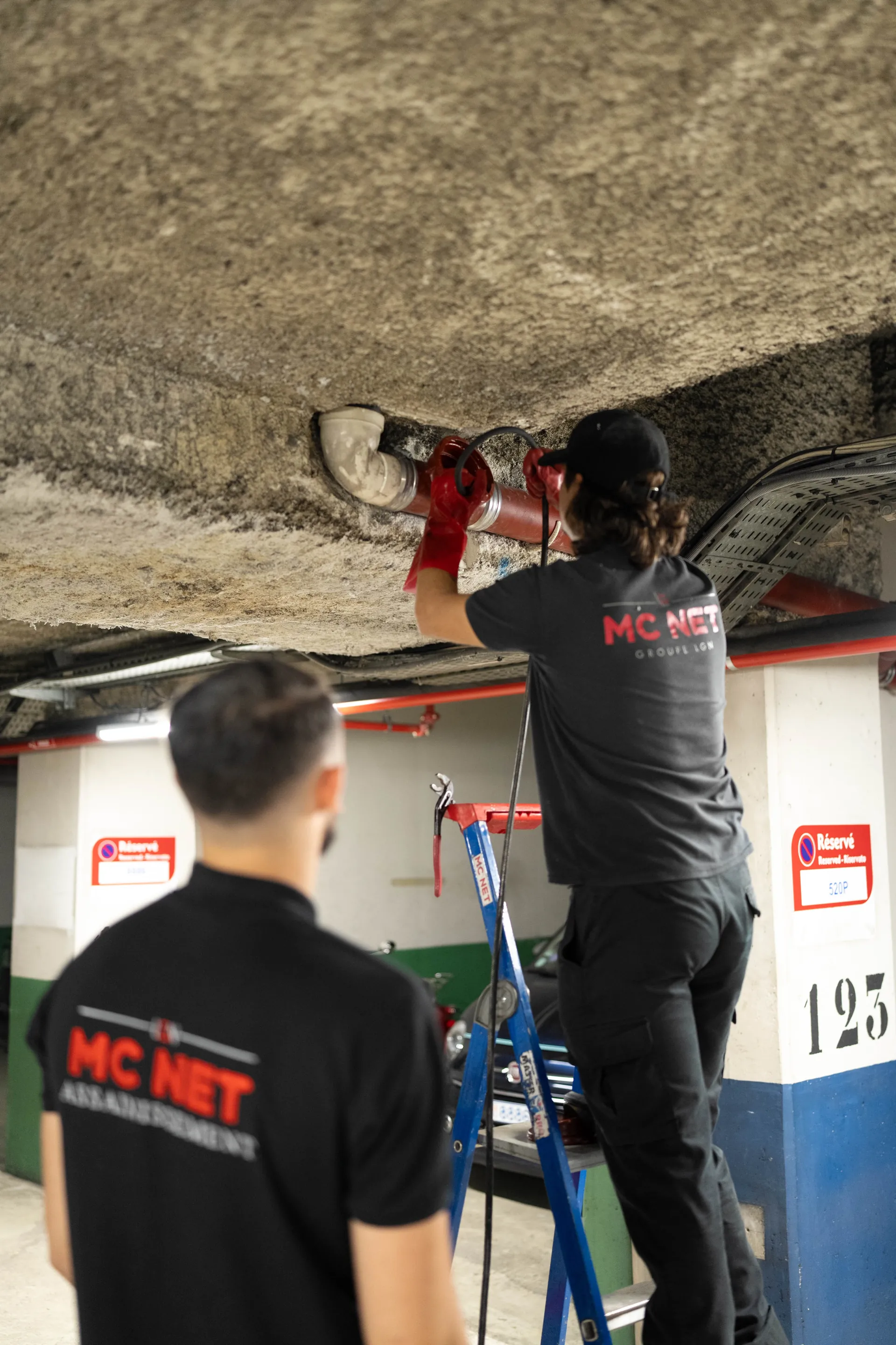 Techniciens MC NET Assainissement intervenant sur une canalisation en parking souterrain